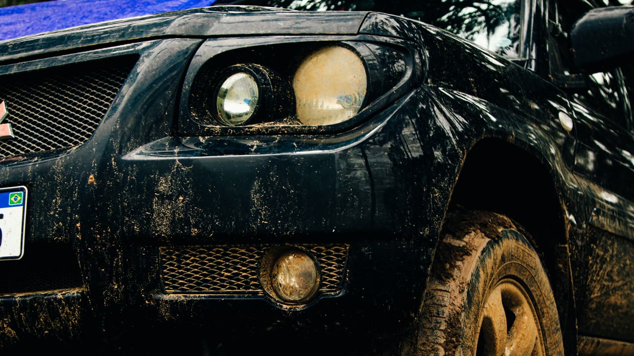 Wet SUV bumper and alloy wheel coated in dull road film and mud after rain.